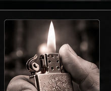 A hand holds an open Zippo lighter with a flame.